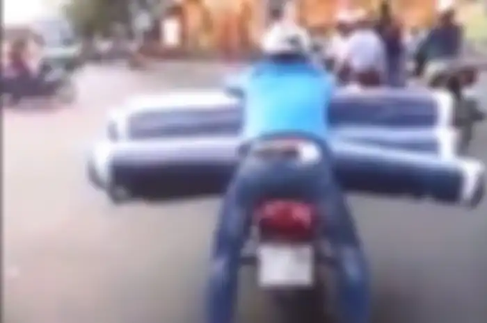Seorang pengendara motor membawa gulungan karpet menggunakan motor, hebat!