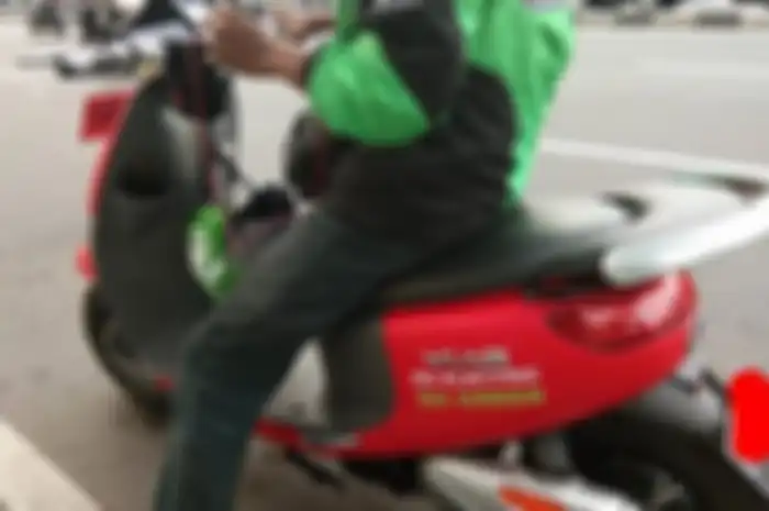 Seorang driver ojek online menggunakan motor listrik.