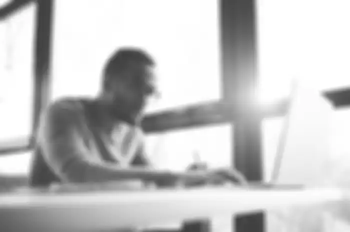 Concentrated dark skinned copywriter in eyewear typing text of publication for web site working on f