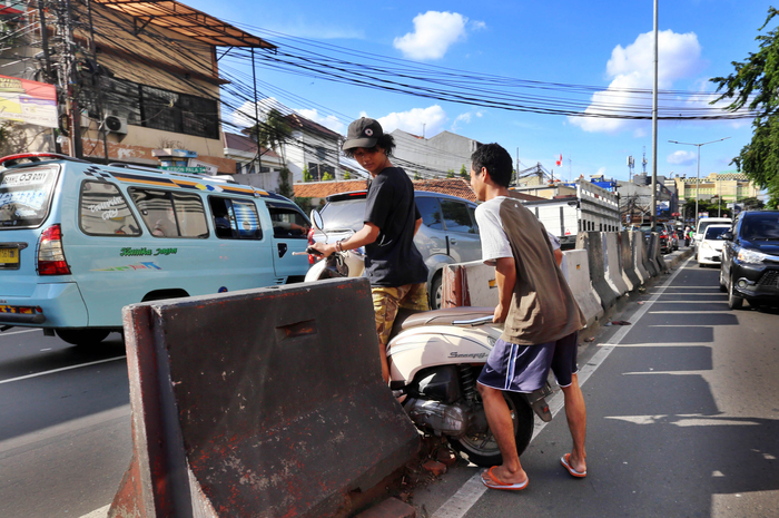 Pengendara sepeda motor dibantu rekannya melintasi separator di Jalan KH Mas Mansyur, Jakarta Pusat,