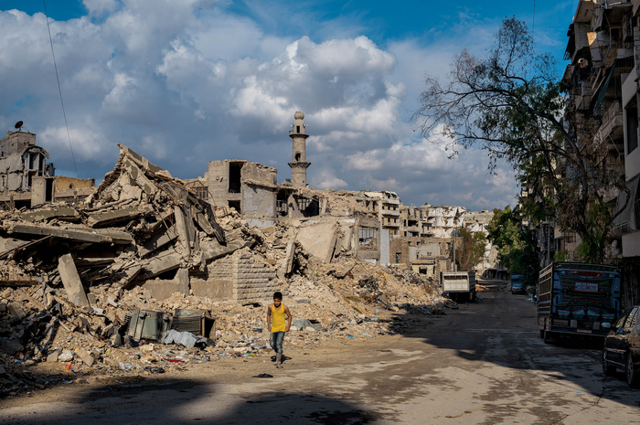 Seorang anak laki-laki berjalan di depan bekas sekolah dan masjid di lingkungan Sukkari di Aleppo selatan. Masjidnya dibangun kembali sementara sebagian besar bangunan di sekitar situ masih berupa reruntuhan.