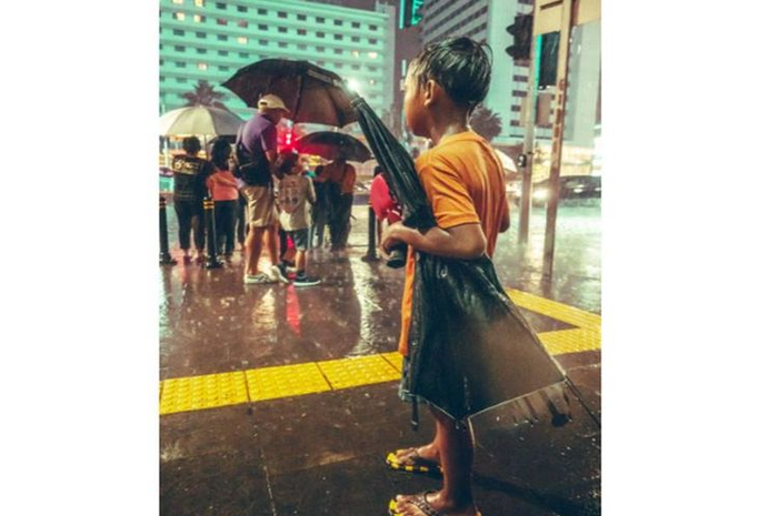 Foto seorang anak yang tengah mencari uang dengan menjadi ojek payung di Jakarta. 