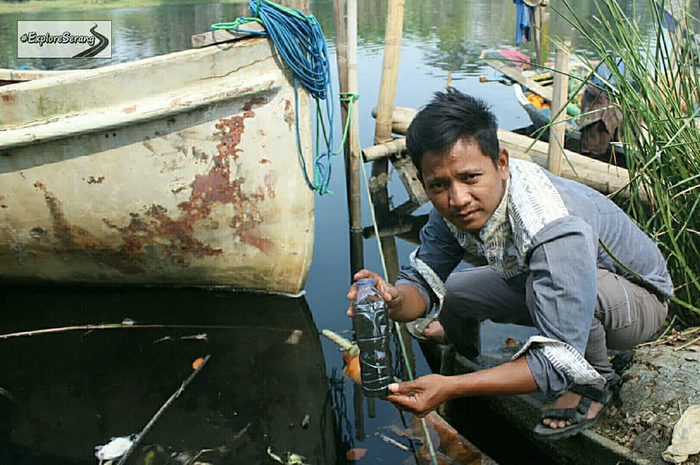 salah satu warga mencoba melihat hitamnya air sungai melalui botol plastik