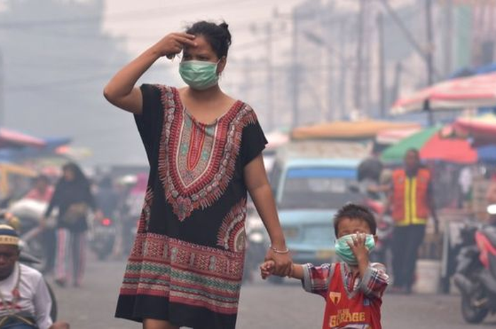 Seorang ibu dan anaknya mengenakan masker saat asap kebakaran hutan dan lahan (Karhutla) menyelimuti Kota Pekanbaru, Riau, Selasa (10/9). 