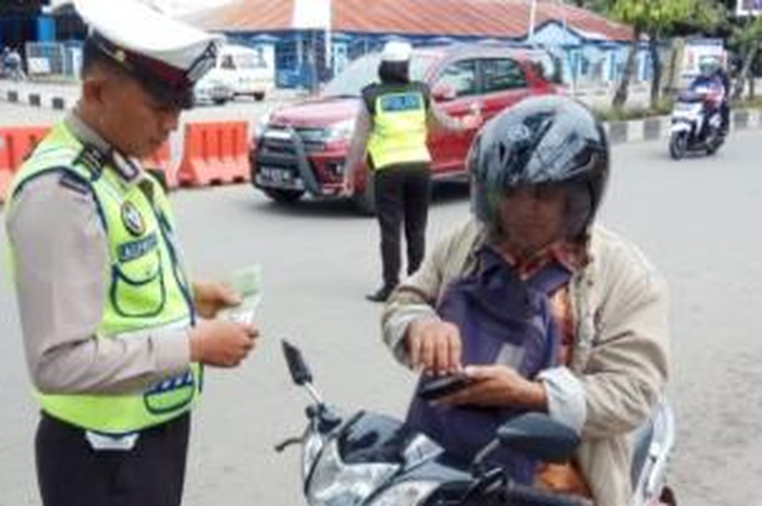 Ilustrasi polisi tilang pengendara motor akibat tidak menyalakan lampu di siang hari.