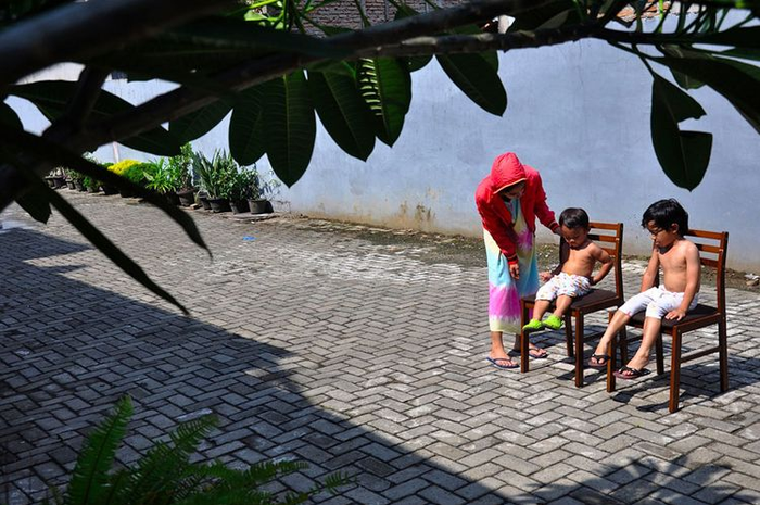 Seorang ibu menjemur kedua anaknya di bawah sinar matahari saat Self Isolation atau tinggal di rumah di Medan, Sumatera Utara, Minggu (22/3/2020). 
