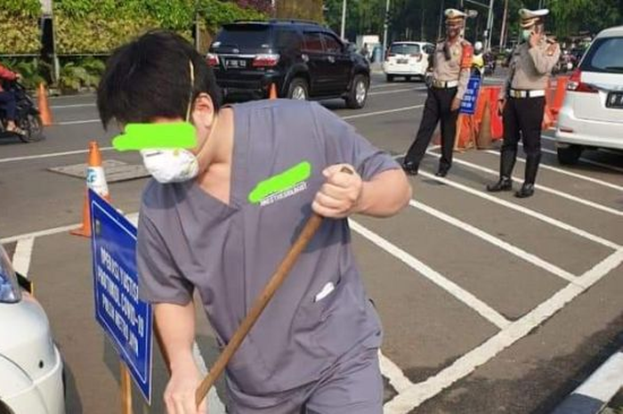 Sosok diduga dokter dihukum polisi menyapu jalan. 