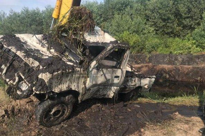 Eskavator mengangkat mobil yang berisi tulang-belulang, di kanal.