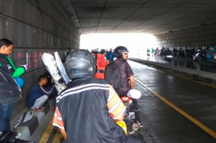 Ilustrasi para pemotor berteduh di underpass saat hujan.