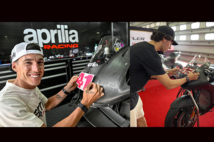 Pembalap MotoGP Aleix Espargaro (kiri) dan Alex Rins melakukan ritual pasang stiker nomor start sendiri di motor barunya, percaya tak percaya biar lebih akrab demi dongkrak performa