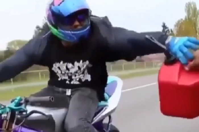 Pengendara motor mengisi bahan bakar saat motornya melaju kencang.