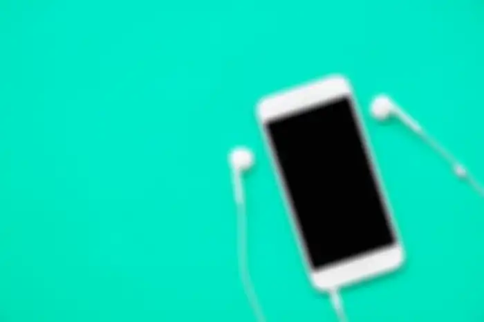 Top view of white mobile phone with headphone on fresh green background