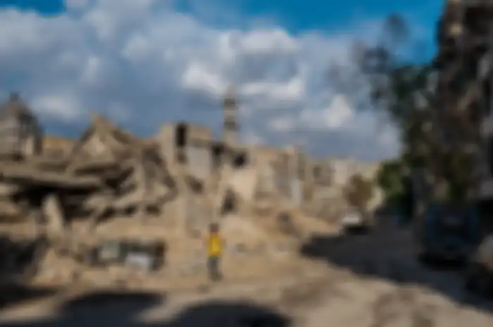 Seorang anak laki-laki berjalan di depan bekas sekolah dan masjid di lingkungan Sukkari di Aleppo selatan. Masjidnya dibangun kembali sementara sebagian besar bangunan di sekitar situ masih berupa reruntuhan.
