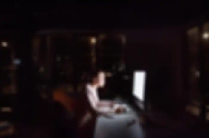 Beautiful young businesswoman in front of computer screen in her office late at night, writing into her personal organizer.