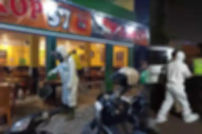 Anggota Tim Kimia Biologi Radioaktif (KBR) Gegana Brimob Polda Jatim menyemprotkan cairan disinfektan ke sebuah warkop berlokasi di Jalan Raya Gunungsari I, Wonokromo, Surabaya, serta membawa pengunjung yang positif Covid-19 ke mobil ambulans 