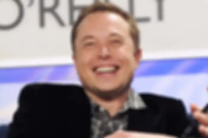 Foto Elon Musk sedang tertawa lebar, Musk mengenakan baju kotak-kotak dan jas berwana hitam.