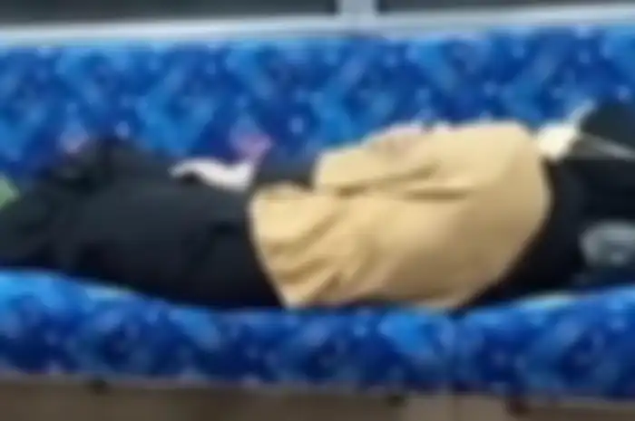 Seorang wanita berhijab sedang berbaring di kursi KRL.