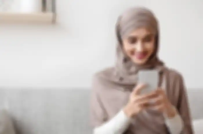 Ilustrasi wanita muslim sedang menunggu waktu buka puasa (ngabuburit) dengan bermain smartphone di Ramdan 2023. 
