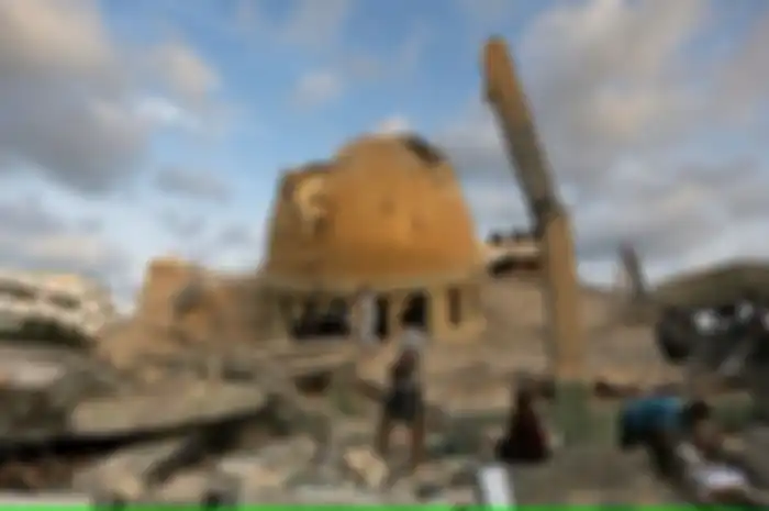 Arti kata ceasefire.(Orang-orang berdiri di luar masjid yang hancur akibat serangan udara Israel di Khan Younis, Jalur Gaza, Minggu, 8 Oktober 2023.)