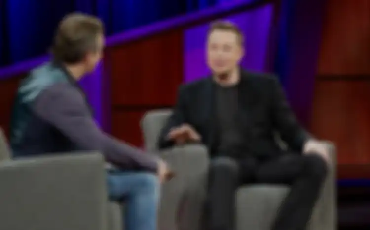 Elon Musk yang memakai pakaian hitam sedang diwawancara oleh seseorang