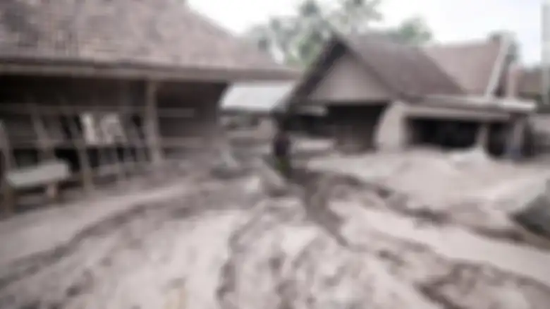 Foto seorang pria berdiri di tengah-tengah dua rumah yang tenggelam karena abu panas gunung Semeru