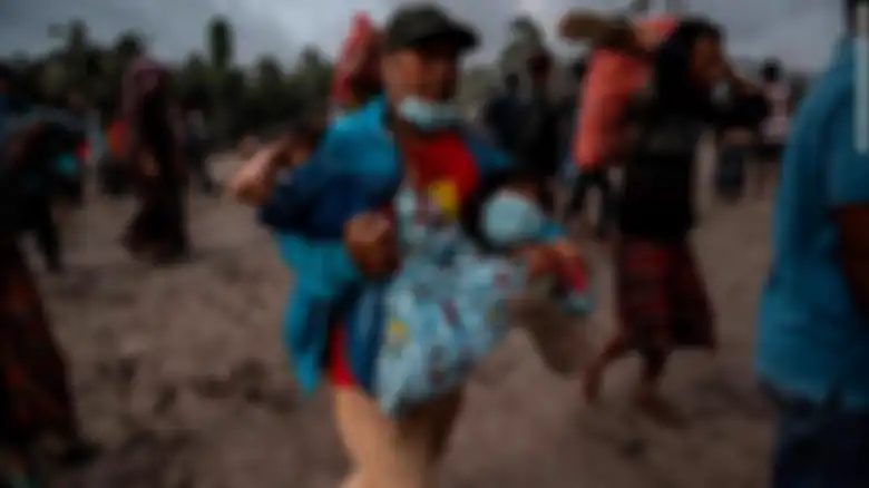 Foto seorang pria membawa anak kecil hari Minggu bersama warga desa lain yang menyelamatkan diri dan harta benda dari tempat tinggal mereka yang terus dihujani abu panas gunung Semeru