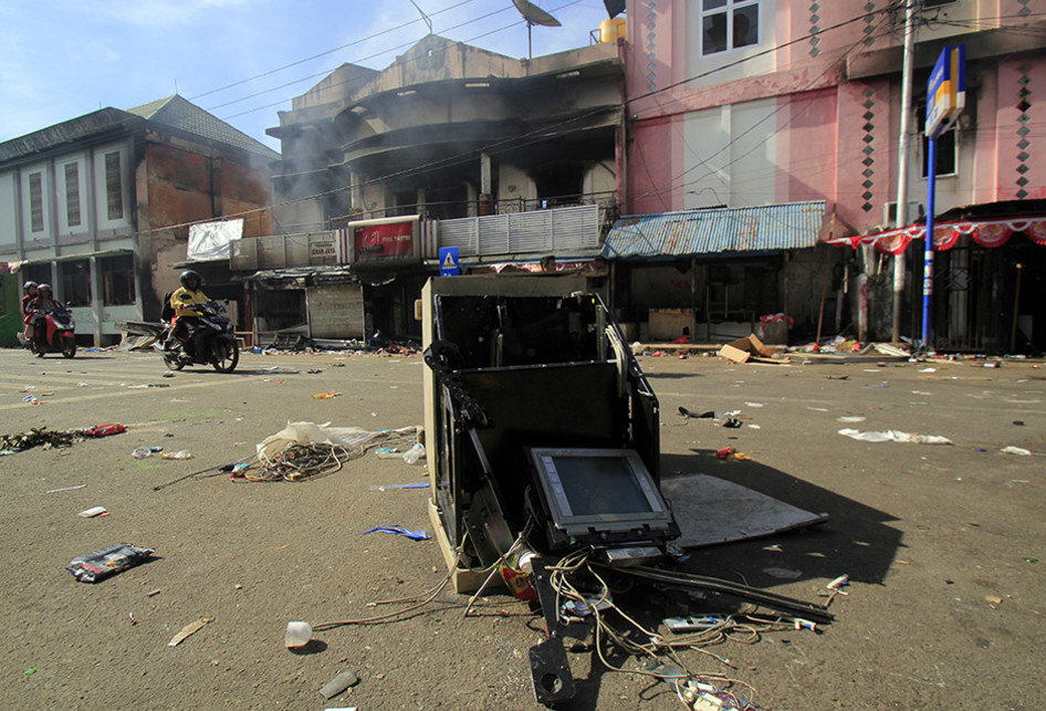 Warga melintasi bangunan dan kendaraan yang rusak, di Jayapura, Papua, Jumat (30/8/2019). Sejumlah bangunan dan kendaraan terbakar saat aksi unjuk rasa yang berakhir rusuh di Jayapura, Kamis kemarin, masih terkait memprotes dugaan tindak rasisme kepada mahasiswa Papua di Jawa Timur beberapa waktu la