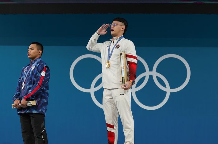 Lifter putra Indonesia, Rizki Juniansyah (tengah) saat upacara pemberian medali setelah meraih medali emas Olimpiade Paris 2024 di kelas 73 kg di South Arena, Paris, Jumat (9/8/2024) dini hari WIB.