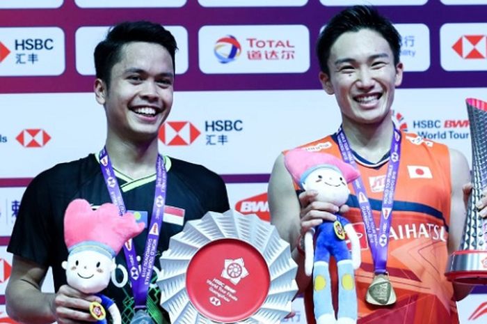 Pebulu tangkis tunggal putra Indonesia, Anthony Sinisuka Ginting (kiri), dan Kento Momota (kanan), berpose di atas podium juara BWF World Tour Finals 2019 di Tianhe Gymnasium, Guangzhou, China, Minggu (15/12/2019).