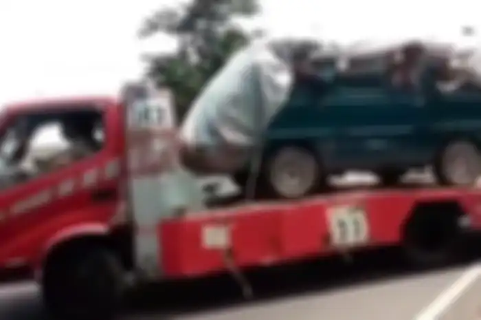 Truk towing yang mengangkut mobil ditutupi terpal yang isinya para pemudik