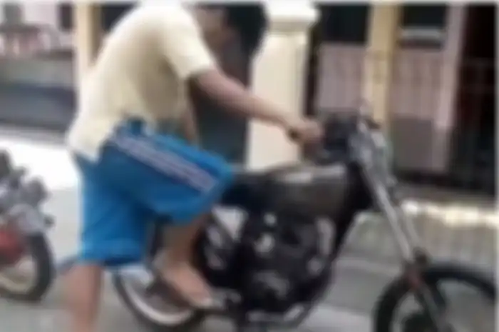 Seorang pemuda mencoba menghidupkan motornya.