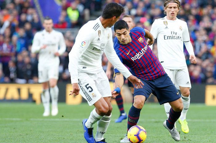 Striker Barcelona, Luis Suarez, berusaha melewati bek Real Madrid, Raphael Varane pada laga El Clasico.