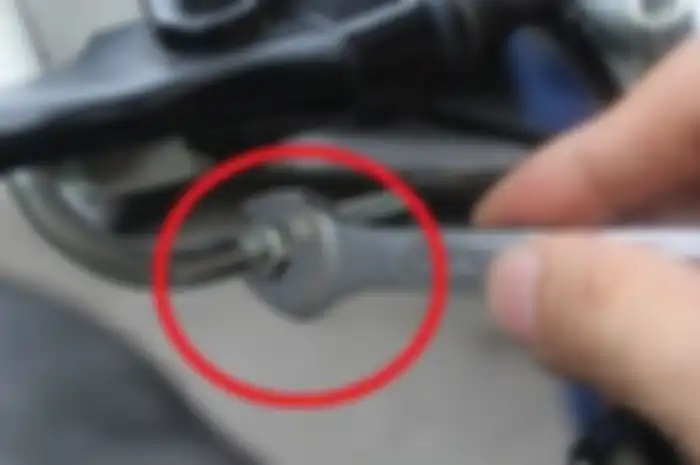 Posisi penyetel ketegangan tali gas ada di bawah selongsong gas.