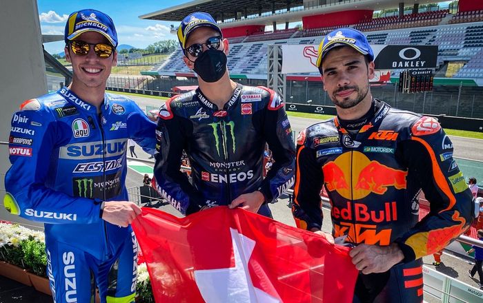 Para penghuni podium MotoGP Italia 2021 (dari kiri ke kanan): Joan Mir, Fabio Quartararo, dan Miguel Oliveira berpose dengan bendera Swiss untuk mengenang mendiang pembalap Moto3, Jason Dupasquier, yang meninggal dunia usai mengalami kecelakaan pada sesi kualifikasi Moto3 Italia 2021.