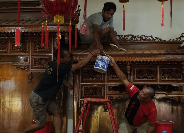 Tiga orang sedang membersihkan altar di Vihara Maha Brahma. Kegiatan ini merupakan bagian dari tradisi Mandi Rupang, yaitu tradisi membersihkan patung dewa dewi dan vihara, yang dilaksanakan beberapa hari sebelum perayaan Hari Imlek.