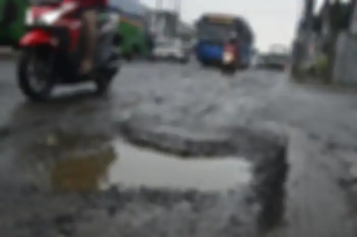 Pemotor melewati jalanan rusak dan berlubang.