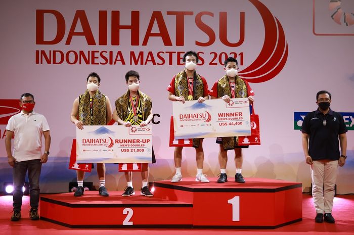 Marcus Fernaldi Gideon/Kevin Sanjaya Sukamuljo (jersey kuning) dan Takuro Hoki/Yugo Kobayashi berbaris di podium setelah final Indonesia Masters 2021 di Bali International Convention Centre, Nusa Dua, Bali, 21 November 2021.