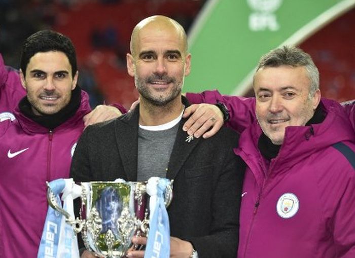 Manajer Manchester City, Pep Guardiola, diapit asistennya, Mikel Arteta (kiri) dan Domenec Torrent, mengangkat trofi Piala Liga Inggris usai menekuk Arsenal di Wembley, London, 25 Februari 2018.