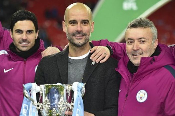 Manajer Manchester City, Pep Guardiola, diapit asistennya, Mikel Arteta (kiri) dan Domenec Torrent, mengangkat trofi Piala Liga Inggris usai menekuk Arsenal di Wembley, London, 25 Februari 2018.